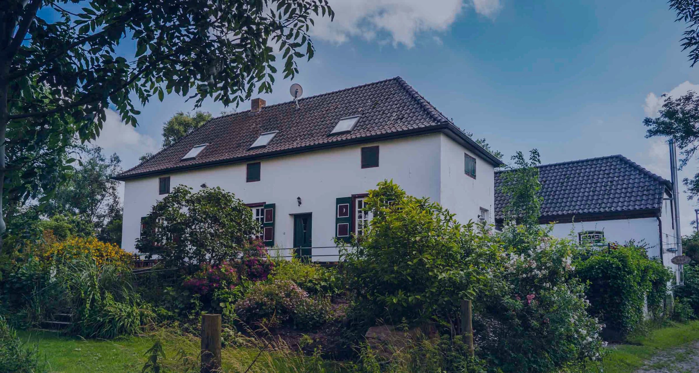 Das weiße Bauernhaus Fristerhof mit grünen Fensterläden, umgeben von einem blühenden Garten