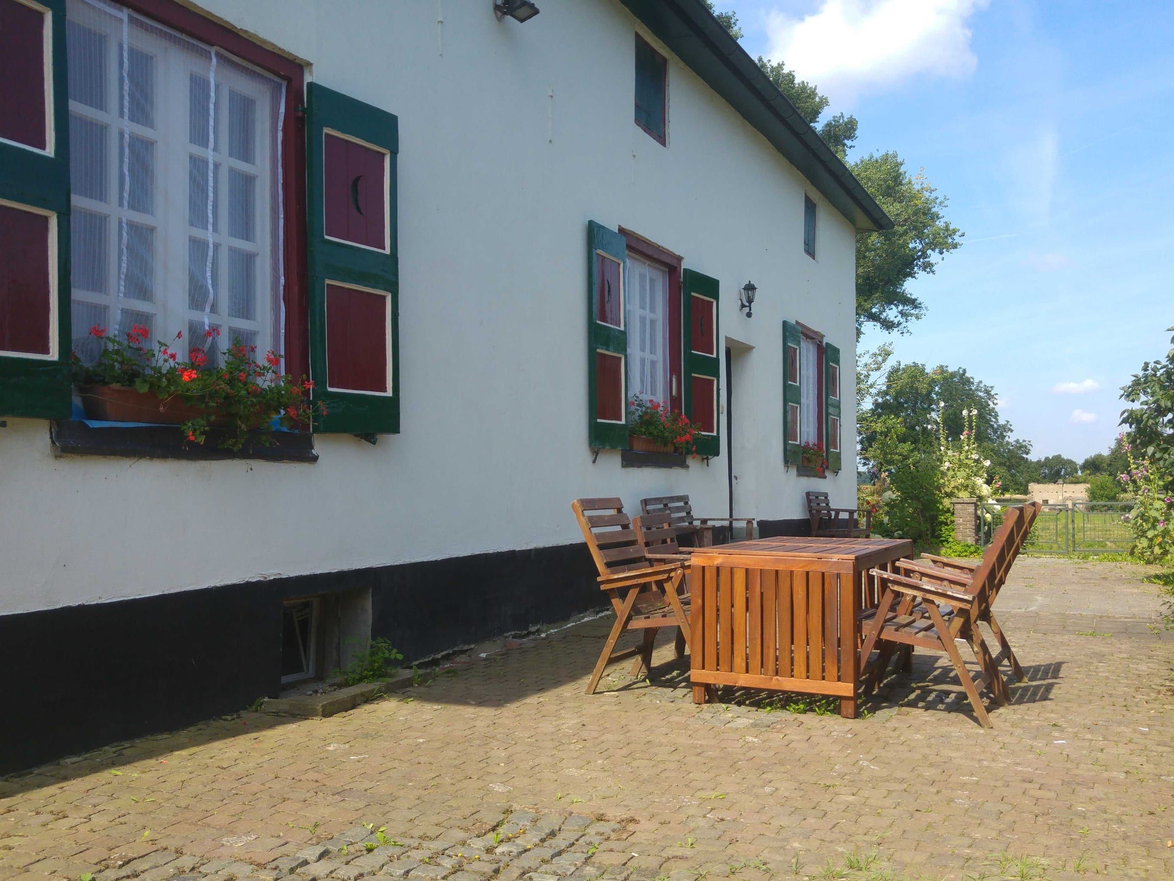 Weiße Fassade mit grünen Fensterläden und roten Fensterrahmen über der Terrasse