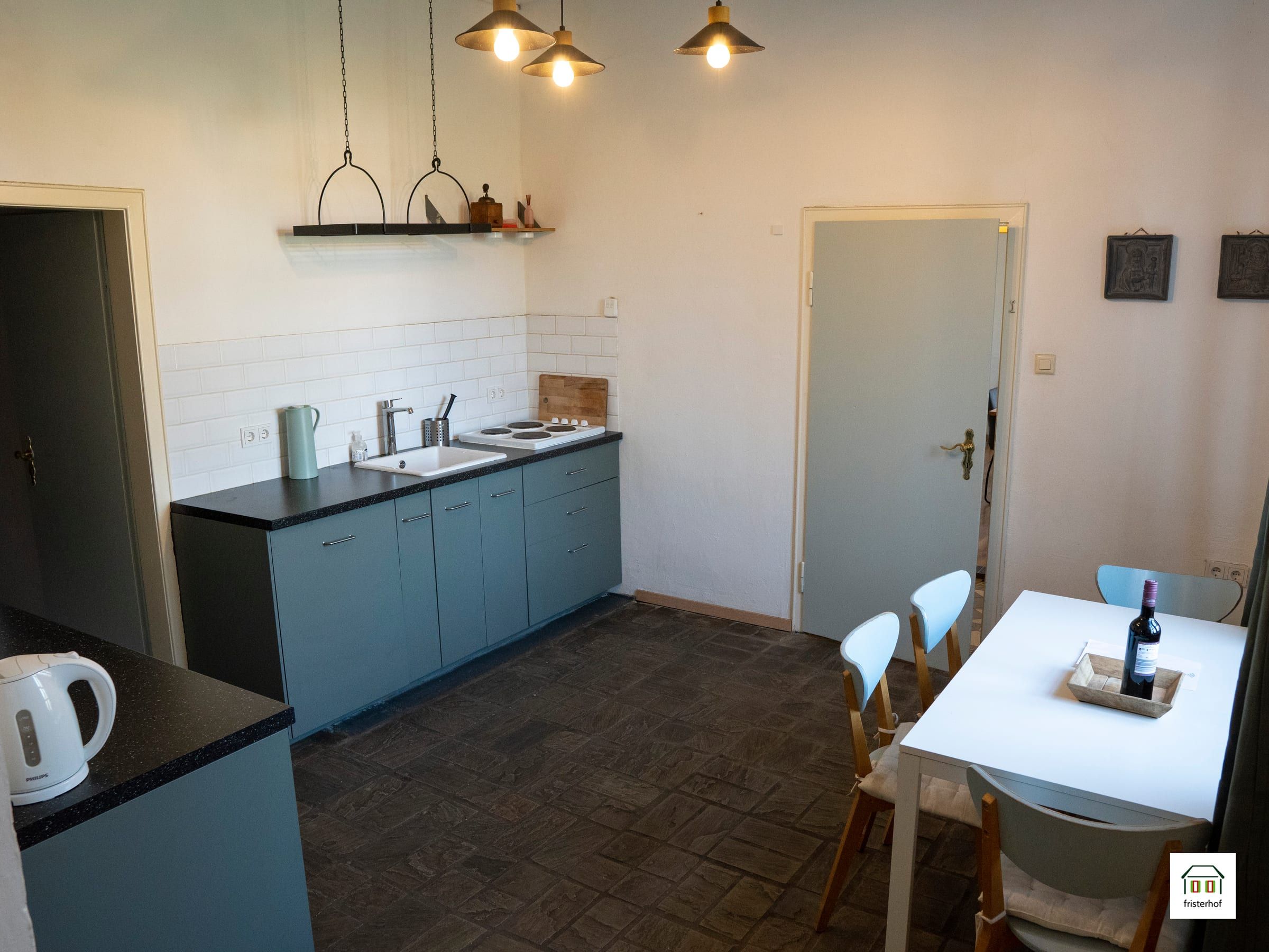 Küche mit hellblauen Schränken und einem weißen Tisch mit Stühlen an der Tür